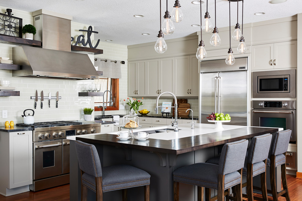 Inspiration for a mid-sized transitional l-shaped kitchen in Minneapolis with an undermount sink, shaker cabinets, quartz benchtops, stainless steel appliances, medium hardwood floors, with island, brown floor, grey cabinets, grey splashback, subway tile splashback and black benchtop.
