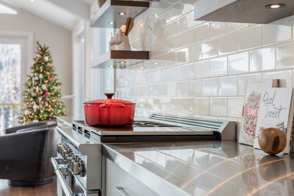 Example of a large transitional single-wall medium tone wood floor eat-in kitchen design with an undermount sink, white cabinets, granite countertops, white backsplash, porcelain backsplash, black appliances, an island and black countertops