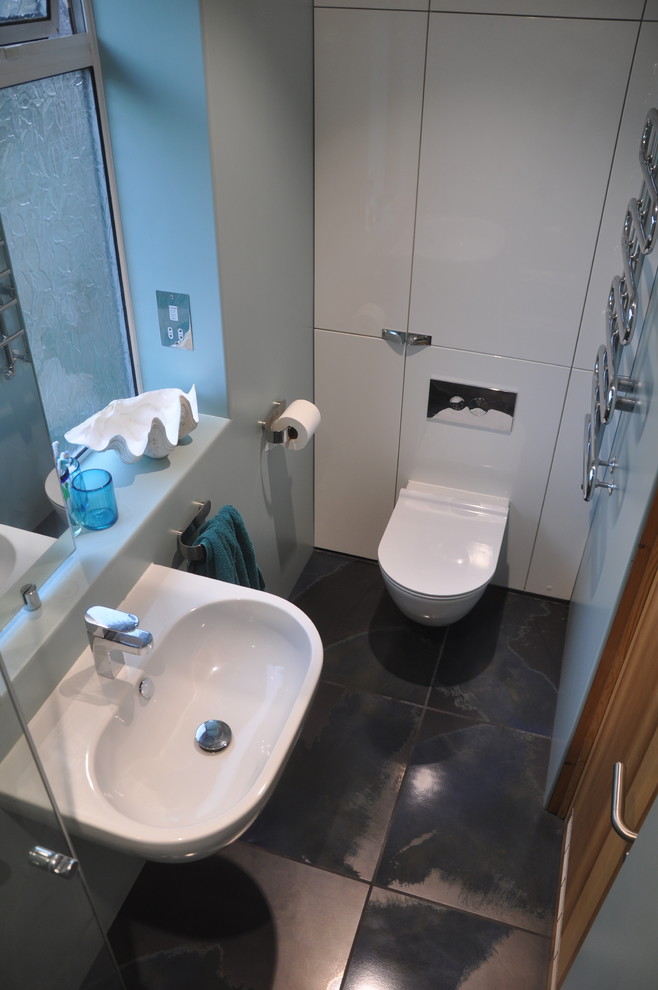 Small modern master wet room bathroom in London with flat-panel cabinets, white cabinets, a wall-mount toilet, green tile, green walls, porcelain floors, a wall-mount sink, laminate benchtops, blue floor, a hinged shower door and green benchtops.