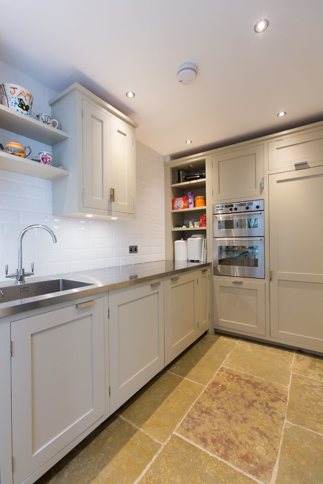 Inspiration for a small contemporary l-shaped open plan kitchen in Surrey with an integrated sink, shaker cabinets, grey cabinets, stainless steel benchtops, white splashback, ceramic splashback, stainless steel appliances and terrazzo floors.