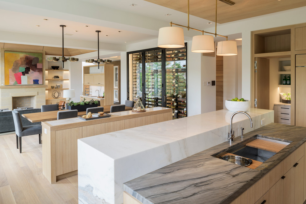 Inspiration for a large modern u-shaped open plan kitchen in Minneapolis with an undermount sink, flat-panel cabinets, light wood cabinets, marble benchtops, white splashback, stone slab splashback, panelled appliances, light hardwood floors and multiple islands.