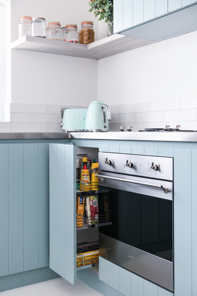 Inspiration for a small beach style l-shaped eat-in kitchen in Sydney with an undermount sink, blue cabinets, stainless steel benchtops, white splashback, subway tile splashback, stainless steel appliances, light hardwood floors, no island, white floor and grey benchtop.