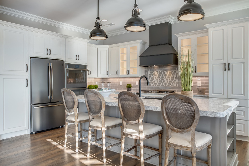 Large transitional l-shaped medium tone wood floor and brown floor open concept kitchen photo with an undermount sink, raised-panel cabinets, white cabinets, quartz countertops, gray backsplash, subway tile backsplash, stainless steel appliances, an island and white countertops
