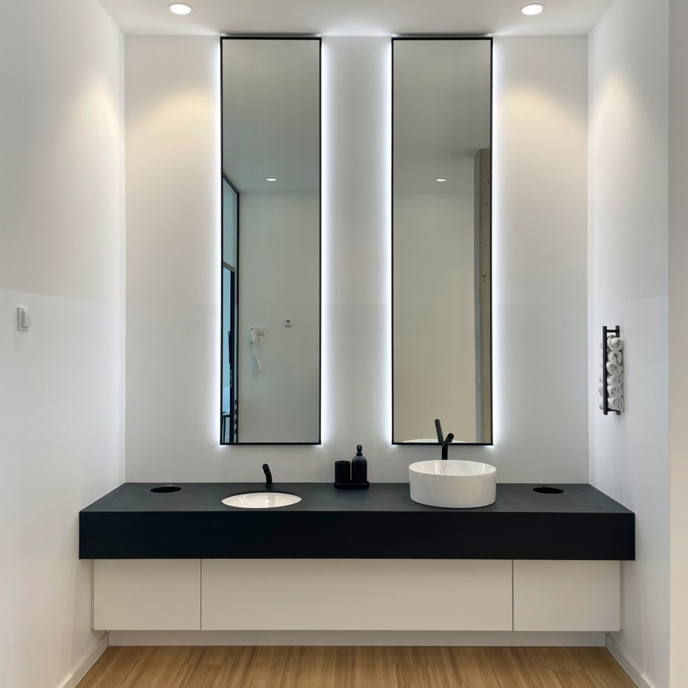 Foto di una piccola stanza da bagno minimalista con ante lisce, ante bianche, pareti bianche, pavimento in bambù, top in cemento, pavimento marrone, top nero, due lavabi e mobile bagno incassato