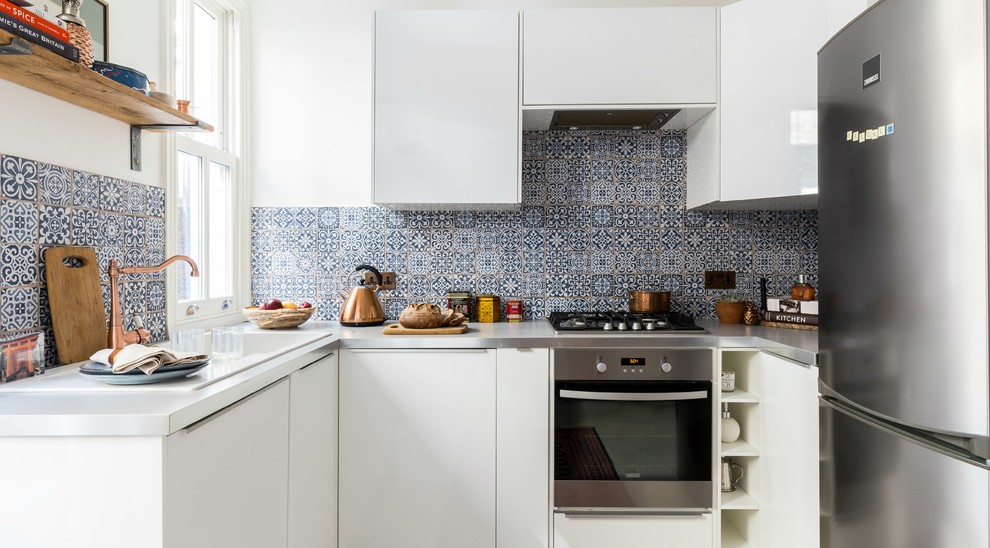 Inspiration for a small contemporary u-shaped separate kitchen in London with a drop-in sink, flat-panel cabinets, white cabinets, black splashback, ceramic splashback, stainless steel appliances, ceramic floors, no island and stainless steel benchtops.