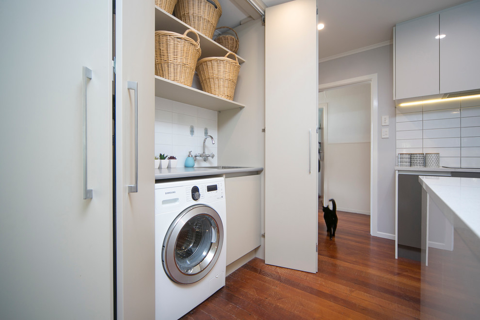 Design ideas for a small modern single-wall laundry cupboard in Auckland with a single-bowl sink, flat-panel cabinets, laminate benchtops and a side-by-side washer and dryer.