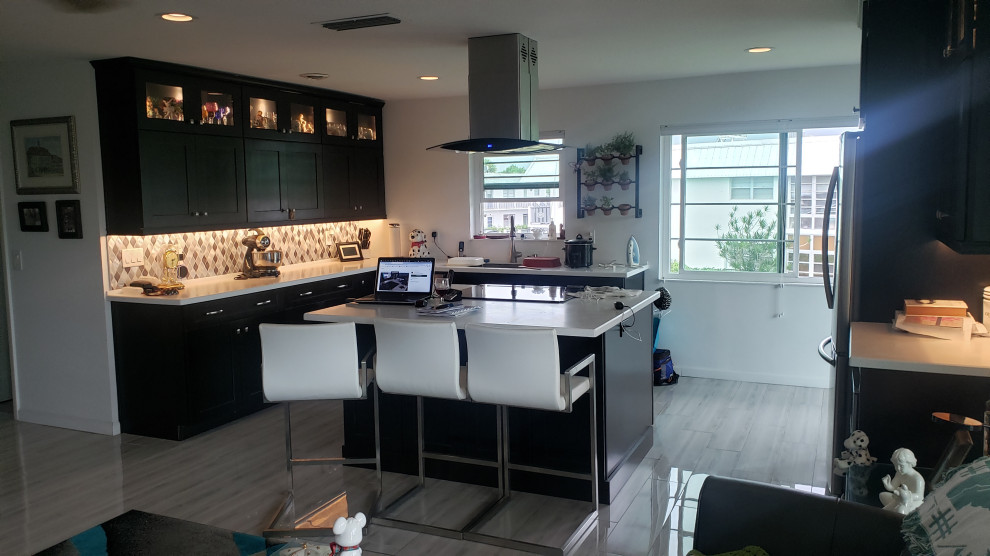 Mid-sized contemporary l-shaped eat-in kitchen in Miami with an undermount sink, shaker cabinets, dark wood cabinets, solid surface benchtops, metal splashback, stainless steel appliances, porcelain floors, with island, grey floor and white benchtop.