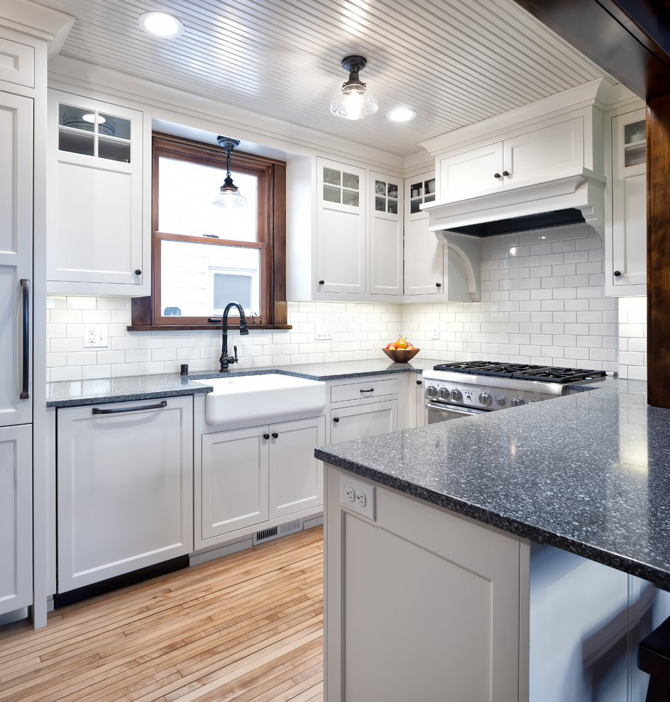 Mid-sized traditional u-shaped eat-in kitchen in Minneapolis with a farmhouse sink, shaker cabinets, white cabinets, recycled glass benchtops, white splashback, subway tile splashback, panelled appliances, light hardwood floors, a peninsula, brown floor and grey benchtop.