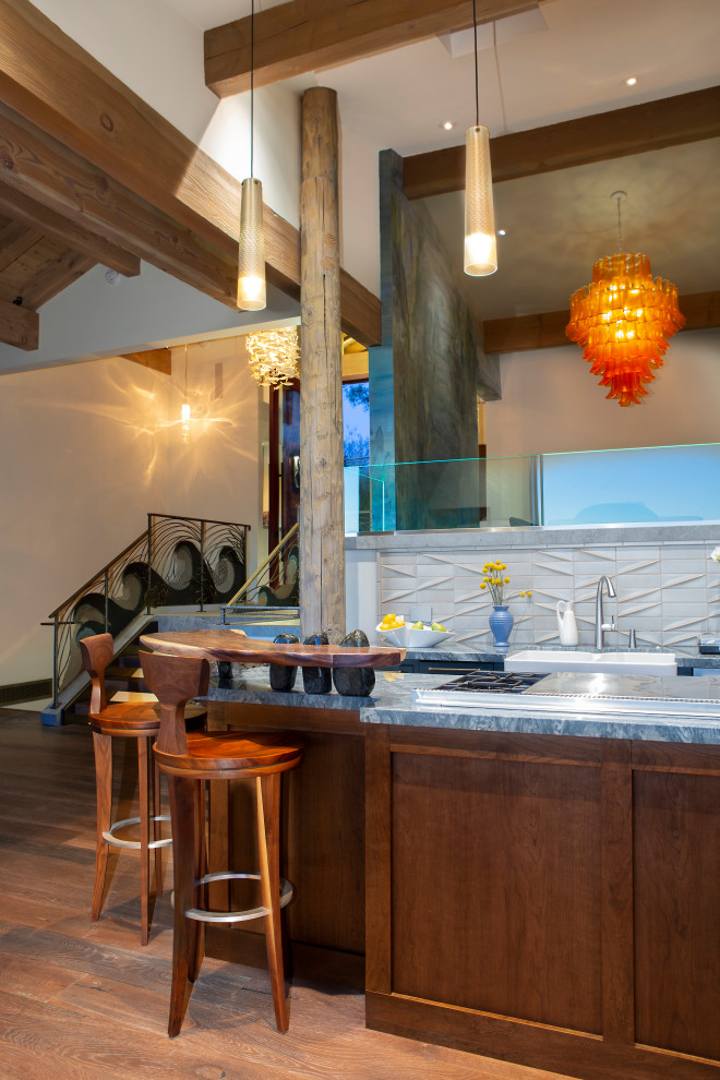 Photo of a mid-sized eclectic galley open plan kitchen in San Diego with a farmhouse sink, beaded inset cabinets, brown cabinets, quartzite benchtops, grey splashback, ceramic splashback, stainless steel appliances, medium hardwood floors, with island, brown floor and blue benchtop.