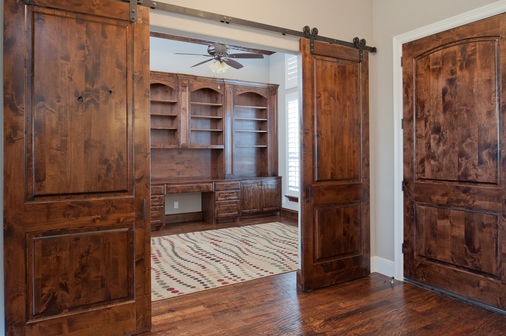 This is an example of a large traditional home office in Dallas with a library, white walls, dark hardwood floors, a built-in desk and brown floor.