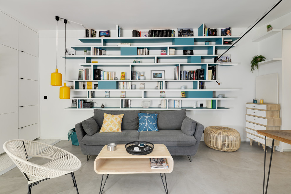 Inspiration for a mid-sized scandinavian open concept living room in Paris with a library, white walls, concrete floors, no fireplace, grey floor and a concealed tv.