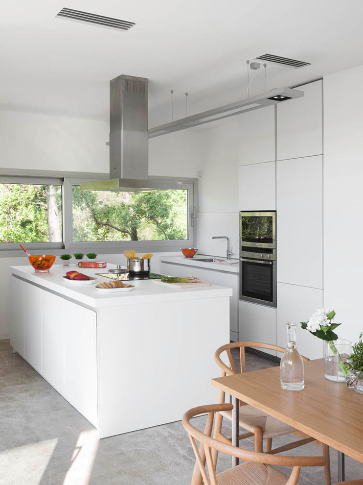 Photo of a mid-sized contemporary u-shaped eat-in kitchen in Other with an undermount sink, flat-panel cabinets, white cabinets, stainless steel appliances, concrete floors, with island, solid surface benchtops and white splashback.