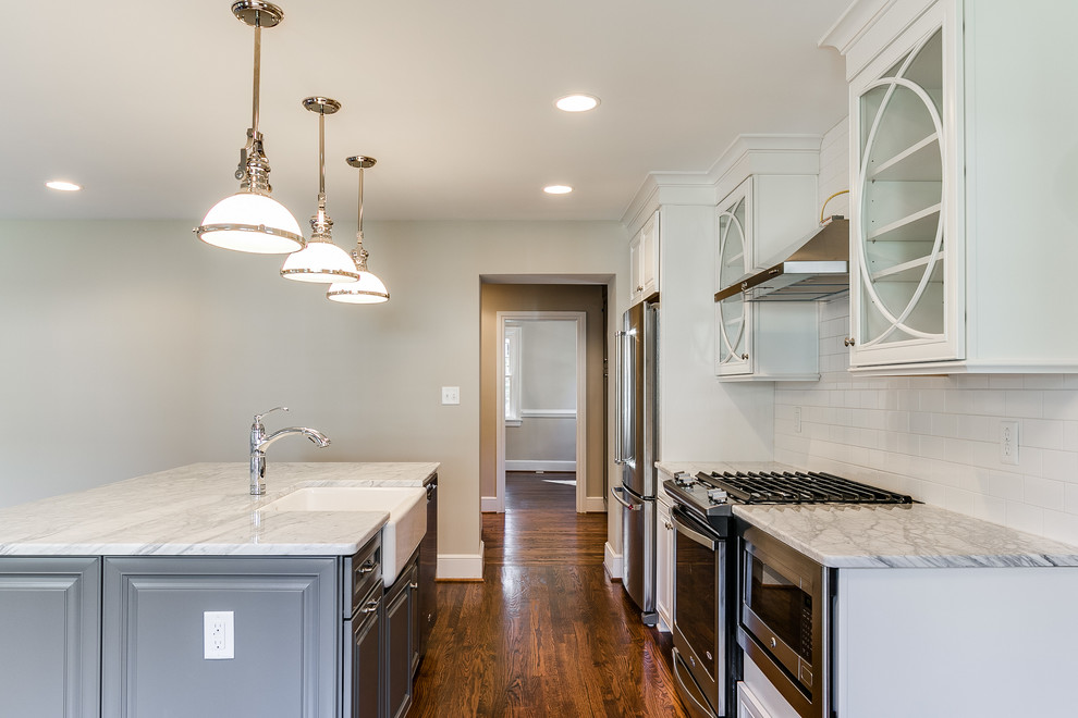 Inspiration for a single-wall medium tone wood floor eat-in kitchen remodel in Richmond with a farmhouse sink, glass-front cabinets, white cabinets, marble countertops, white backsplash, subway tile backsplash, stainless steel appliances and an island