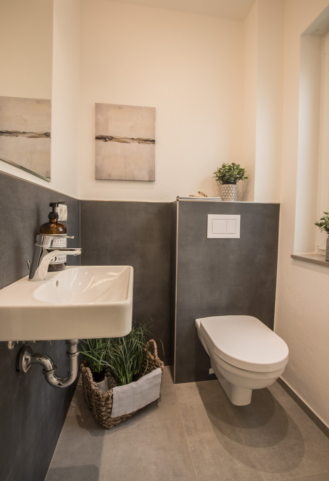 Mittelgroße Moderne Gästetoilette mit Wandtoilette, grauen Fliesen, weißer Wandfarbe, Keramikboden, Wandwaschbecken und grauem Boden in Bonn