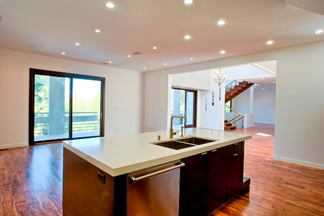 Example of a large minimalist l-shaped medium tone wood floor eat-in kitchen design in Los Angeles with a single-bowl sink, flat-panel cabinets, dark wood cabinets, granite countertops, white backsplash, glass sheet backsplash, stainless steel appliances, white walls and an island