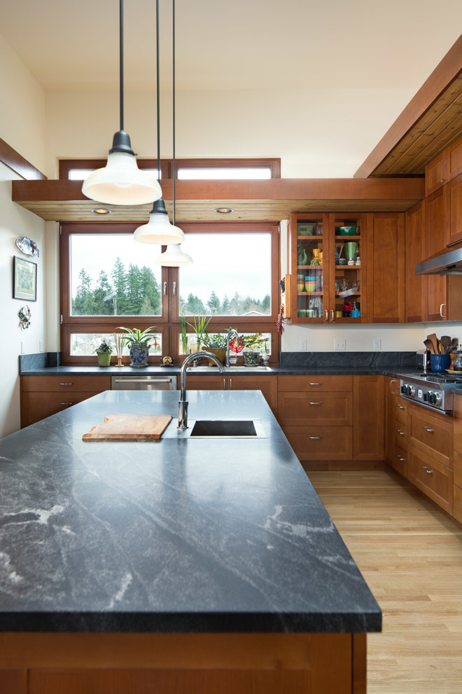 Photo of a modern u-shaped kitchen in Seattle with a drop-in sink, shaker cabinets, medium wood cabinets, soapstone benchtops, stainless steel appliances, light hardwood floors, with island, beige floor and black benchtop.