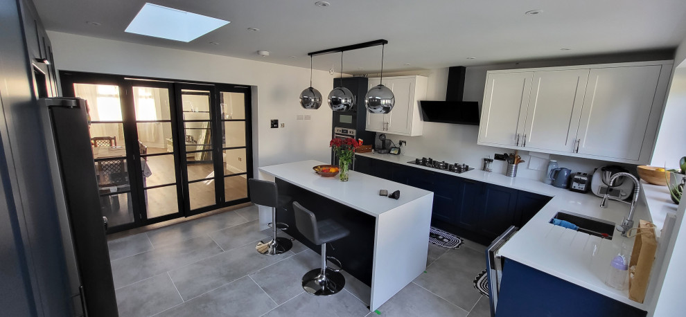 Enclosed kitchen - large contemporary u-shaped porcelain tile and gray floor enclosed kitchen idea in London with a drop-in sink, beaded inset cabinets, blue cabinets, quartz countertops, white backsplash, stone slab backsplash, black appliances, an island and white countertops