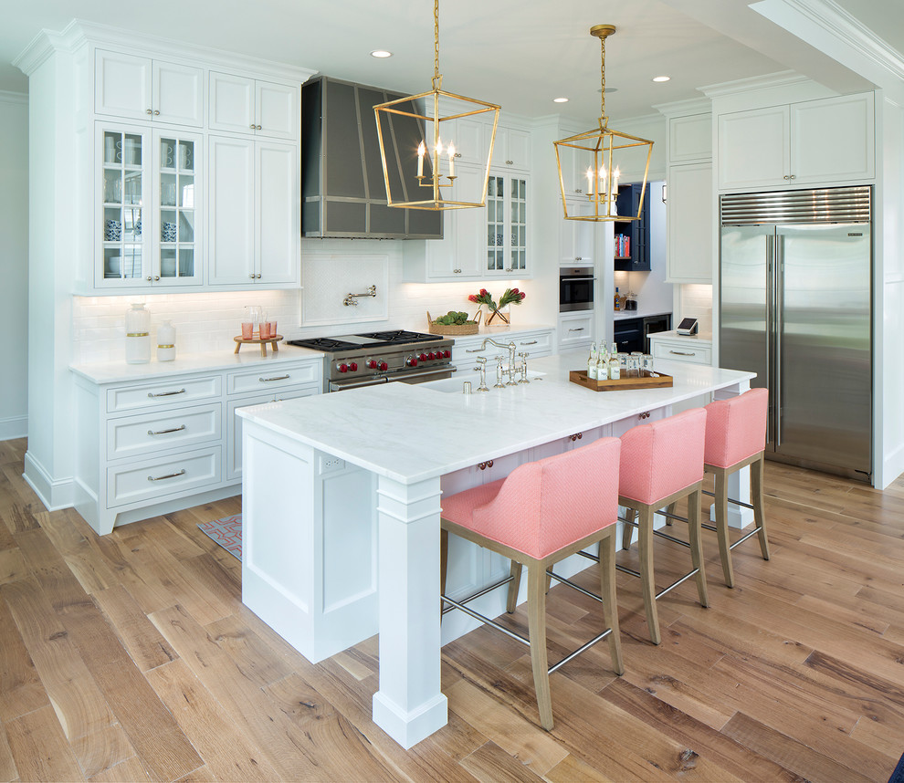 Inspiration for a mid-sized transitional galley light wood floor open concept kitchen remodel in Minneapolis with a farmhouse sink, white cabinets, marble countertops, white backsplash, subway tile backsplash, stainless steel appliances, an island, recessed-panel cabinets and white countertops