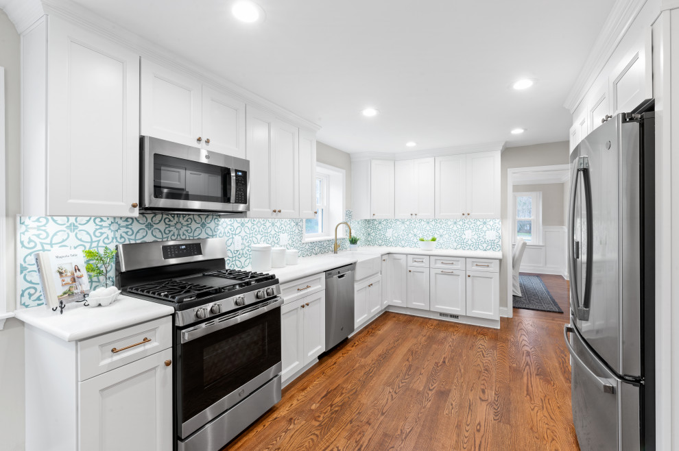 Photo of a medium sized country l-shaped kitchen/diner in Philadelphia with a belfast sink, shaker cabinets, white cabinets, quartz worktops, blue splashback, stainless steel appliances, medium hardwood flooring and white worktops.