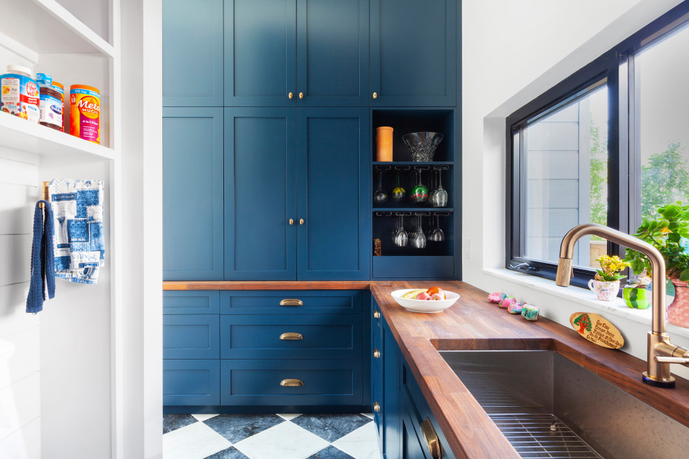 Modern inredning av ett mellanstort brun brunt kök, med en undermonterad diskho, skåp i shakerstil, blå skåp, träbänkskiva, vitt stänkskydd, integrerade vitvaror, klinkergolv i porslin och svart golv