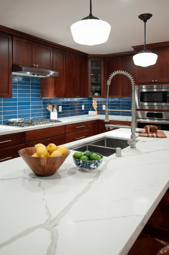 Photo of a large transitional l-shaped eat-in kitchen in San Francisco with a double-bowl sink, shaker cabinets, brown cabinets, blue splashback, glass tile splashback, stainless steel appliances, light hardwood floors, with island, yellow floor and white benchtop.
