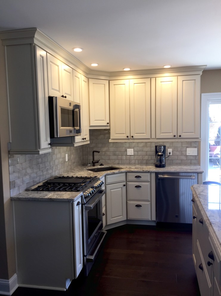 Inspiration for a large rustic u-shaped dark wood floor and brown floor eat-in kitchen remodel in Atlanta with an undermount sink, raised-panel cabinets, beige cabinets, granite countertops, beige backsplash, glass tile backsplash, stainless steel appliances, an island and multicolored countertops