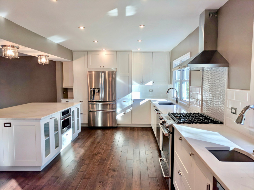 Inspiration for a large classic l-shaped kitchen/diner in Seattle with a submerged sink, white cabinets, engineered stone countertops, white splashback, ceramic splashback, stainless steel appliances, medium hardwood flooring, an island and white worktops.