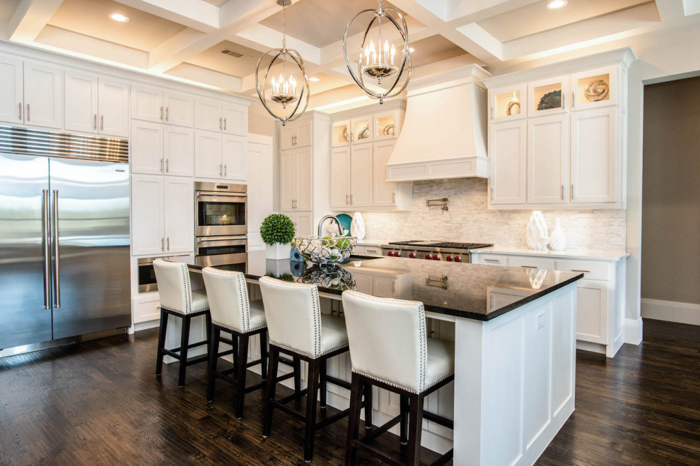 This is an example of a large transitional l-shaped eat-in kitchen in Dallas with a drop-in sink, raised-panel cabinets, white cabinets, granite benchtops, white splashback, stone tile splashback, stainless steel appliances, dark hardwood floors, with island, brown floor and black benchtop.