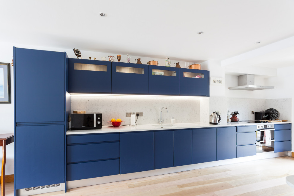 Large contemporary single-wall kitchen in Cork with an undermount sink, flat-panel cabinets, blue cabinets, grey splashback, stainless steel appliances, light hardwood floors, no island, beige floor and white benchtop.