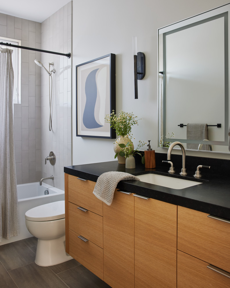 Transitional bathroom in Los Angeles with flat-panel cabinets, medium wood cabinets, an alcove tub, a shower/bathtub combo, gray tile, white walls, a wall-mount sink, grey floor, a shower curtain, black benchtops, a single vanity and a floating vanity.