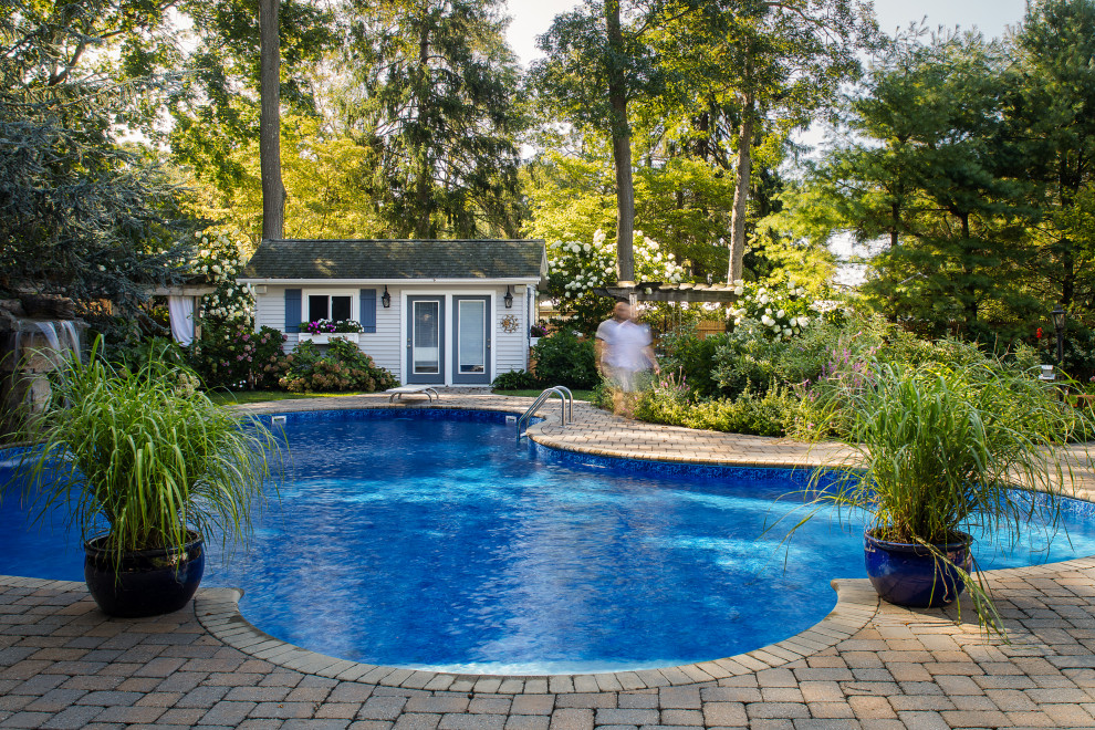На фото: бассейн среднего размера, в форме фасоли на заднем дворе в стиле неоклассика (современная классика) с домиком у бассейна и мощением клинкерной брусчаткой