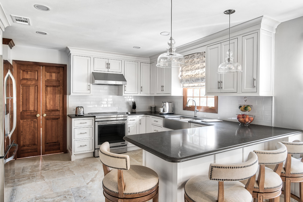 Example of a large transitional u-shaped beige floor kitchen design in New York with a farmhouse sink, white cabinets, white backsplash, subway tile backsplash, stainless steel appliances, a peninsula, black countertops and shaker cabinets