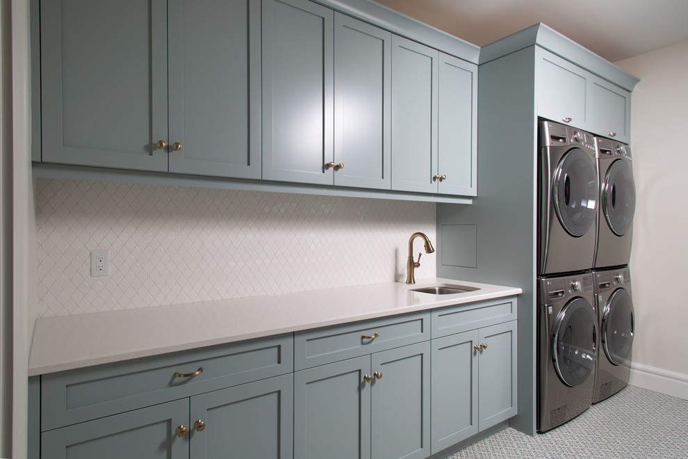 Large transitional single-wall dedicated laundry room in Toronto with shaker cabinets, blue cabinets, quartz benchtops, white walls, linoleum floors, a stacked washer and dryer, multi-coloured floor, white benchtop and an undermount sink.