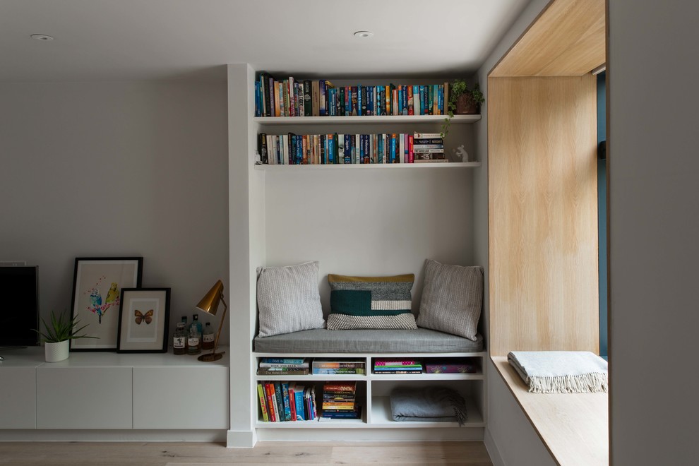 Small modern open concept living room in London with a library, light hardwood floors and white walls.