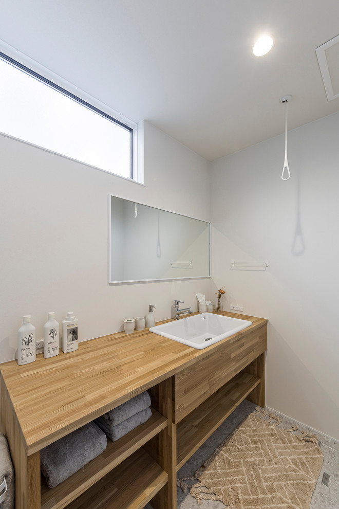 Modern powder room in Other with open cabinets, medium wood cabinets, gray tile, white walls, terra-cotta floors, a drop-in sink, wood benchtops, grey floor, brown benchtops, a built-in vanity, wallpaper and wallpaper.