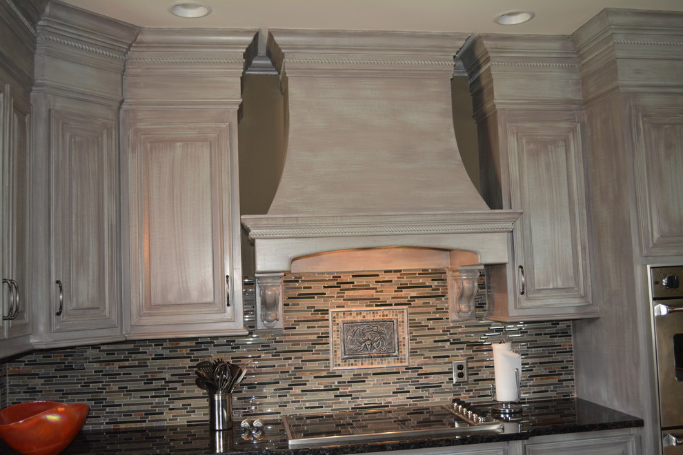 Inspiration for a mid-sized transitional l-shaped enclosed kitchen remodel with raised-panel cabinets, distressed cabinets, granite countertops, beige backsplash, matchstick tile backsplash, stainless steel appliances and an island