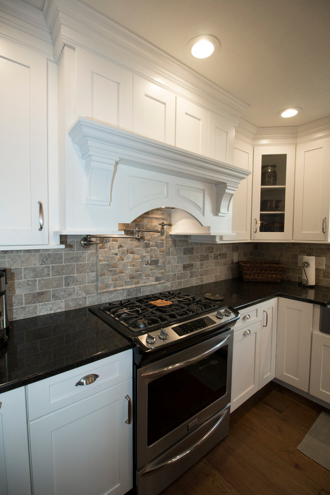Large transitional l-shaped medium tone wood floor eat-in kitchen photo with an undermount sink, shaker cabinets, white cabinets, granite countertops, gray backsplash, stone tile backsplash, stainless steel appliances and an island