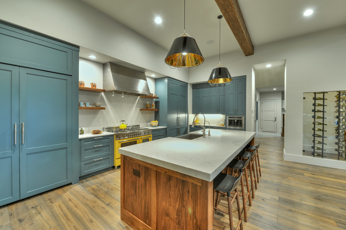 This is an example of a transitional kitchen in Austin with a farmhouse sink, shaker cabinets, blue cabinets, grey splashback, medium hardwood floors, with island and coloured appliances.