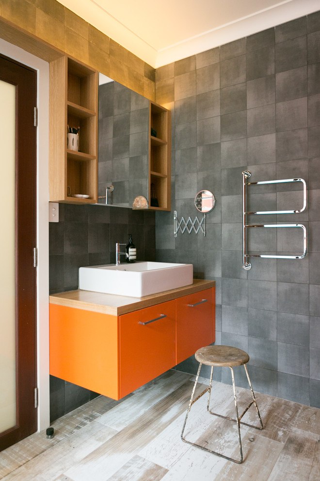 This is an example of a midcentury 3/4 bathroom in Sydney with flat-panel cabinets, orange cabinets, gray tile, grey walls, light hardwood floors, a vessel sink, wood benchtops and brown benchtops.