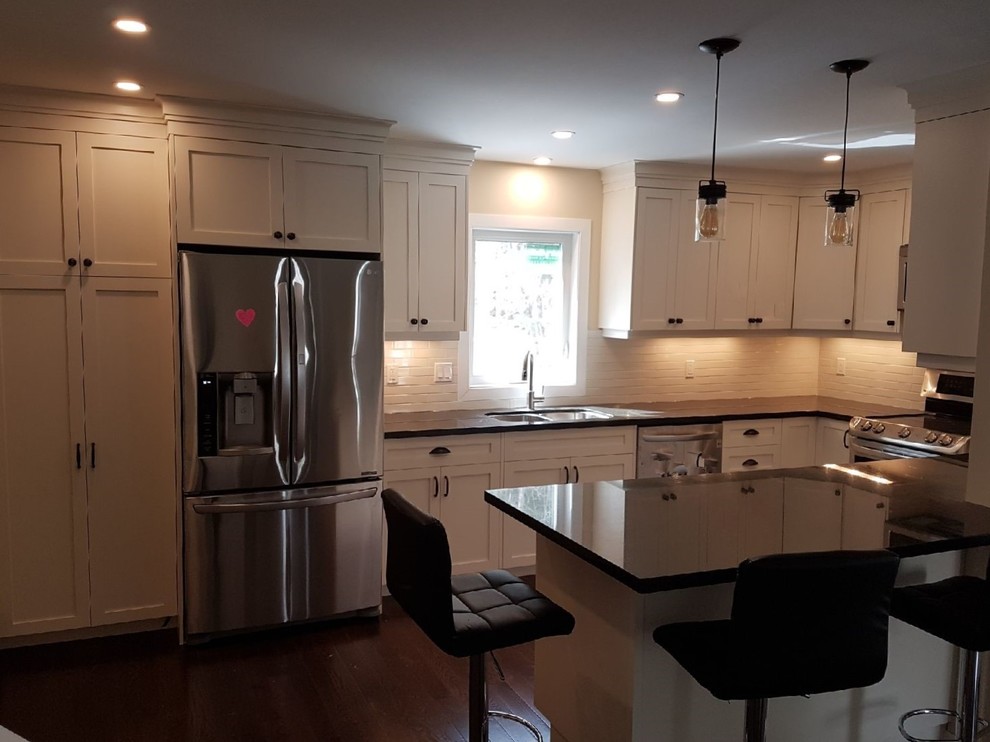 This is an example of a mid-sized arts and crafts u-shaped eat-in kitchen in Toronto with an undermount sink, shaker cabinets, white cabinets, granite benchtops, white splashback, ceramic splashback, stainless steel appliances, medium hardwood floors, a peninsula and brown floor.