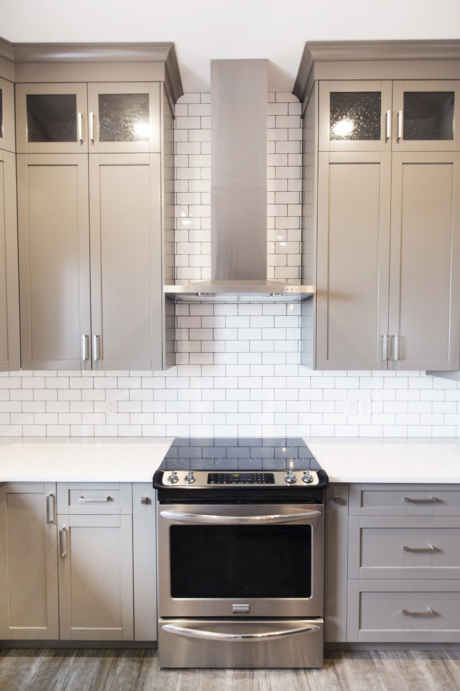 Example of a transitional laminate floor kitchen design in Calgary with gray cabinets, white backsplash, subway tile backsplash, stainless steel appliances and an island