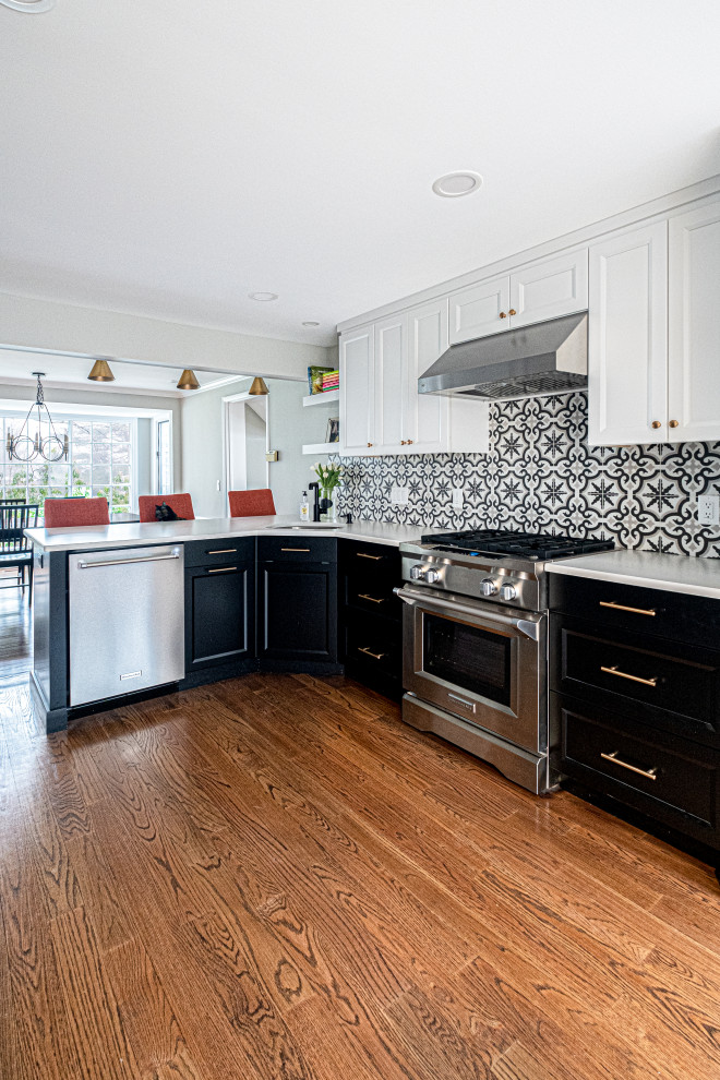 This is an example of a mid-sized transitional l-shaped eat-in kitchen in Newark with an undermount sink, black cabinets, quartzite benchtops, multi-coloured splashback, porcelain splashback, stainless steel appliances, medium hardwood floors, a peninsula, white benchtop and shaker cabinets.