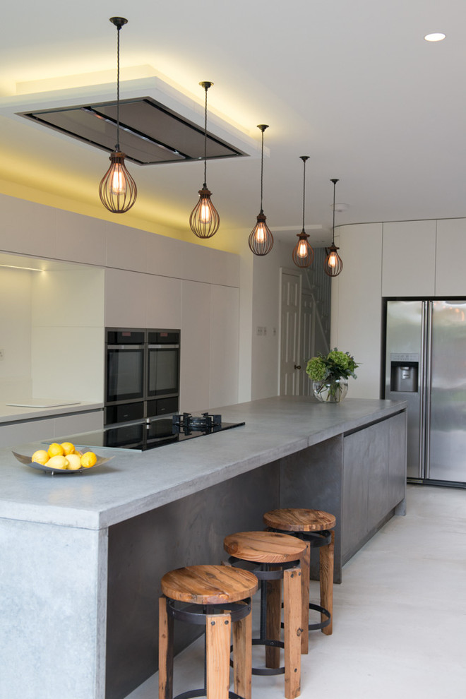 Inspiration for a contemporary galley open plan kitchen in London with flat-panel cabinets, white cabinets, concrete benchtops and stainless steel appliances.