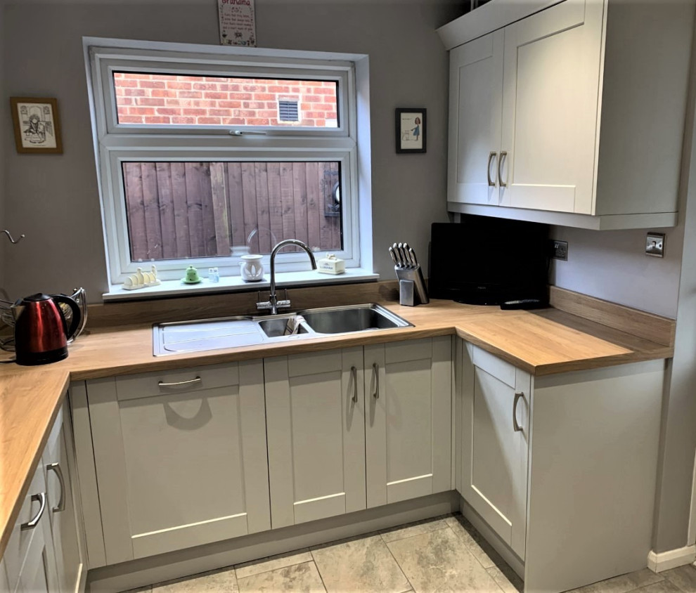 Photo of a mid-sized traditional u-shaped separate kitchen in Other with shaker cabinets, grey cabinets, yellow splashback, glass sheet splashback, black appliances, porcelain floors, no island and grey floor.