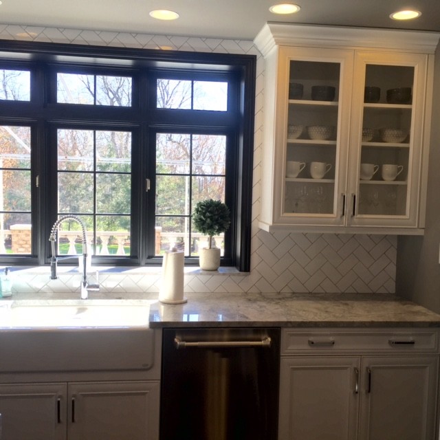 This is an example of a transitional kitchen in Philadelphia with a farmhouse sink, recessed-panel cabinets, white cabinets, marble benchtops, white splashback, ceramic splashback, stainless steel appliances, medium hardwood floors and with island.