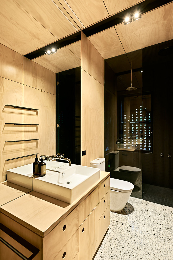 Photo of a small contemporary 3/4 bathroom in Melbourne with a vessel sink, furniture-like cabinets, light wood cabinets, wood benchtops, a curbless shower, a one-piece toilet, black tile, mosaic tile, beige walls and concrete floors.