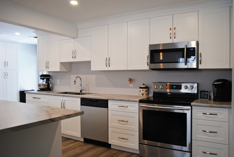 Example of a mid-sized transitional medium tone wood floor and brown floor kitchen pantry design with a drop-in sink, shaker cabinets, white cabinets, laminate countertops, beige backsplash, stainless steel appliances, an island and gray countertops