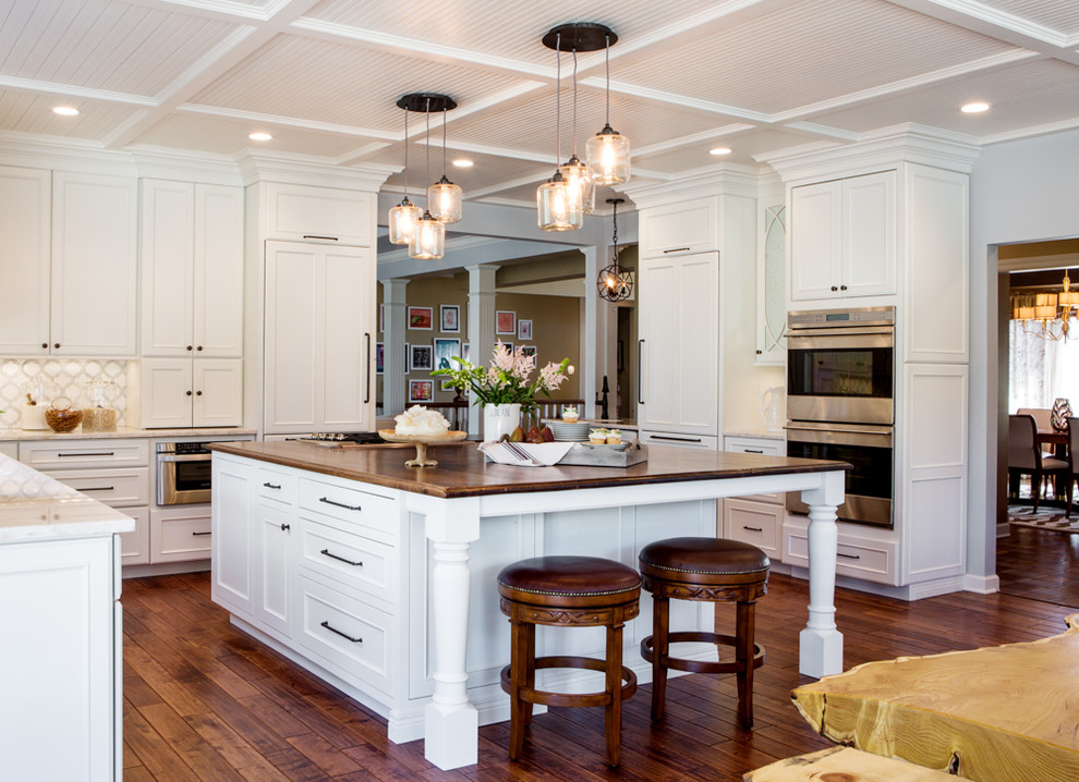 Traditional u-shaped kitchen in St Louis with recessed-panel cabinets, white cabinets, wood benchtops, white splashback, stainless steel appliances, dark hardwood floors and with island.