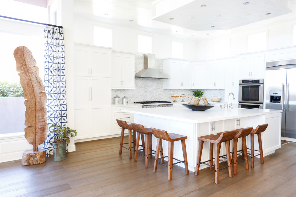 Inspiration for a large beach style l-shaped open plan kitchen in Orange County with a drop-in sink, shaker cabinets, white cabinets, quartz benchtops, grey splashback, mosaic tile splashback, stainless steel appliances, dark hardwood floors and with island.