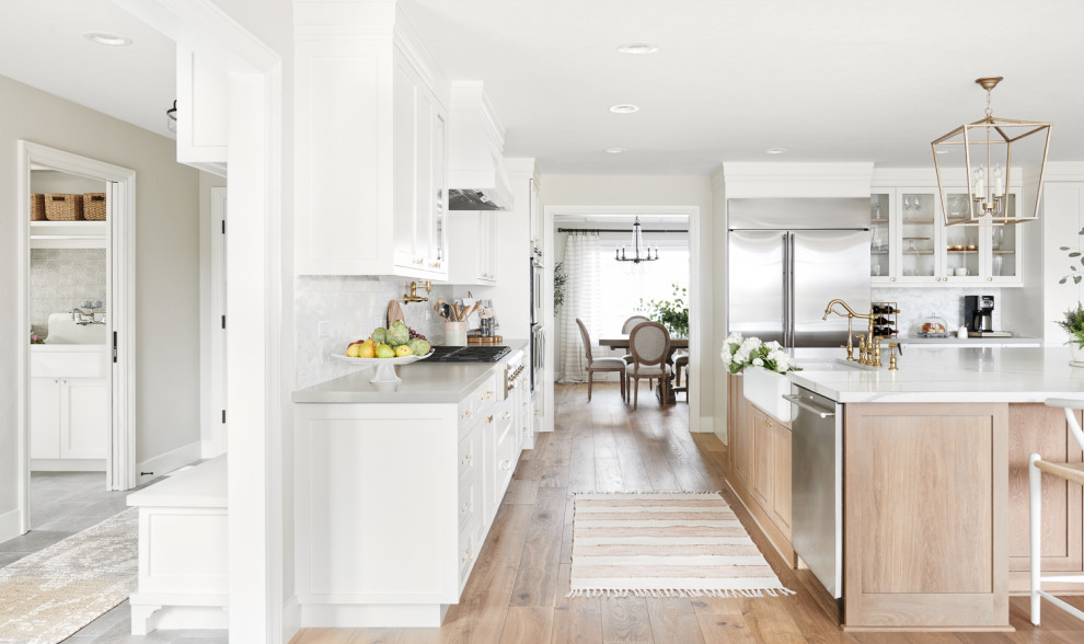 This is an example of a large scandinavian u-shaped eat-in kitchen in San Francisco with a farmhouse sink, recessed-panel cabinets, white cabinets, quartzite benchtops, white splashback, marble splashback, stainless steel appliances, light hardwood floors, with island, beige floor and white benchtop.